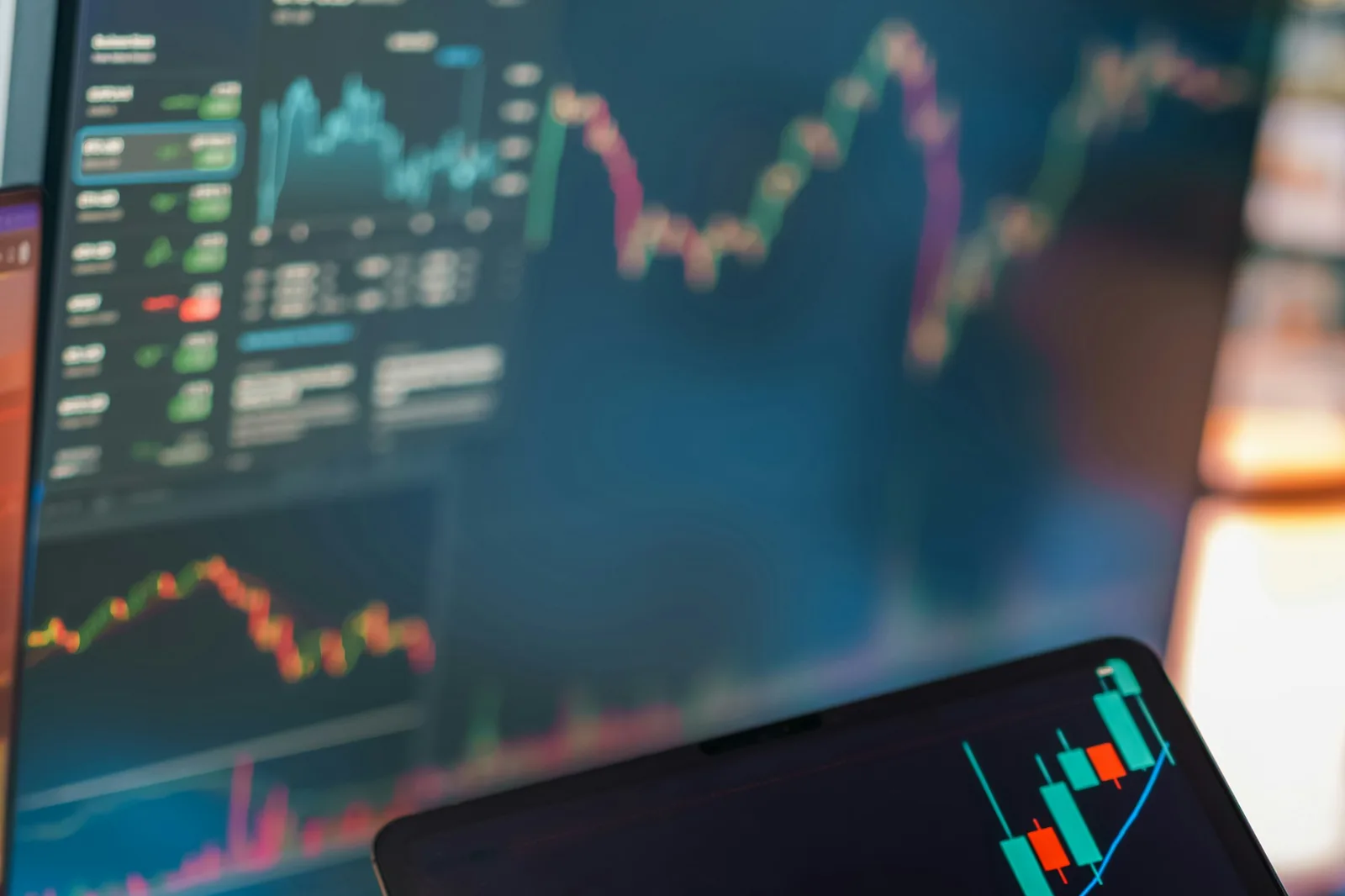 Trading charts and data displayed across multiple screens and a tablet on a desk