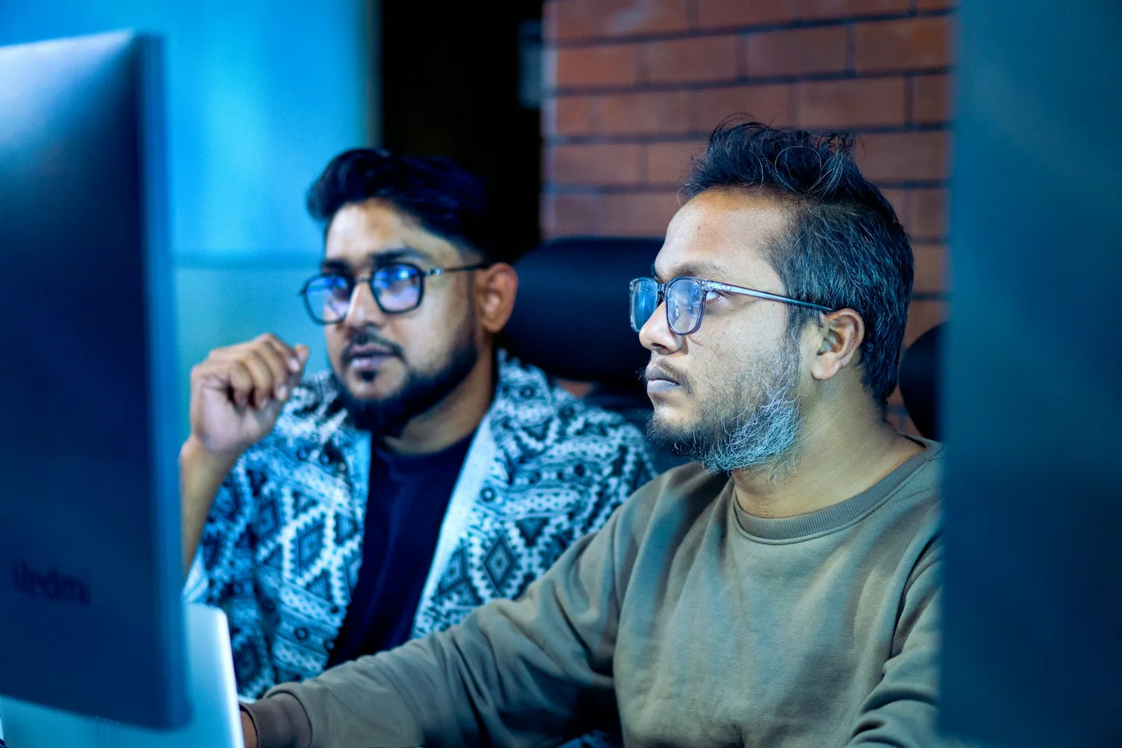 Two colleagues looking intently at a computer screen while reviewing work together