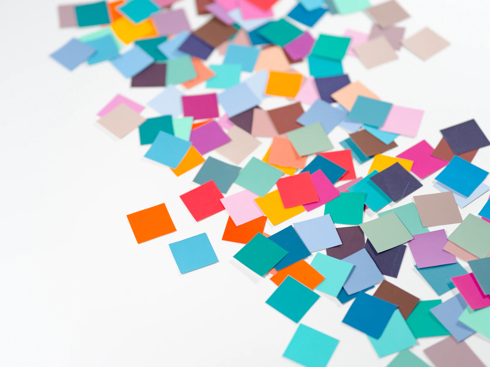 A pile of multicoloured paper confetti squares on a white table