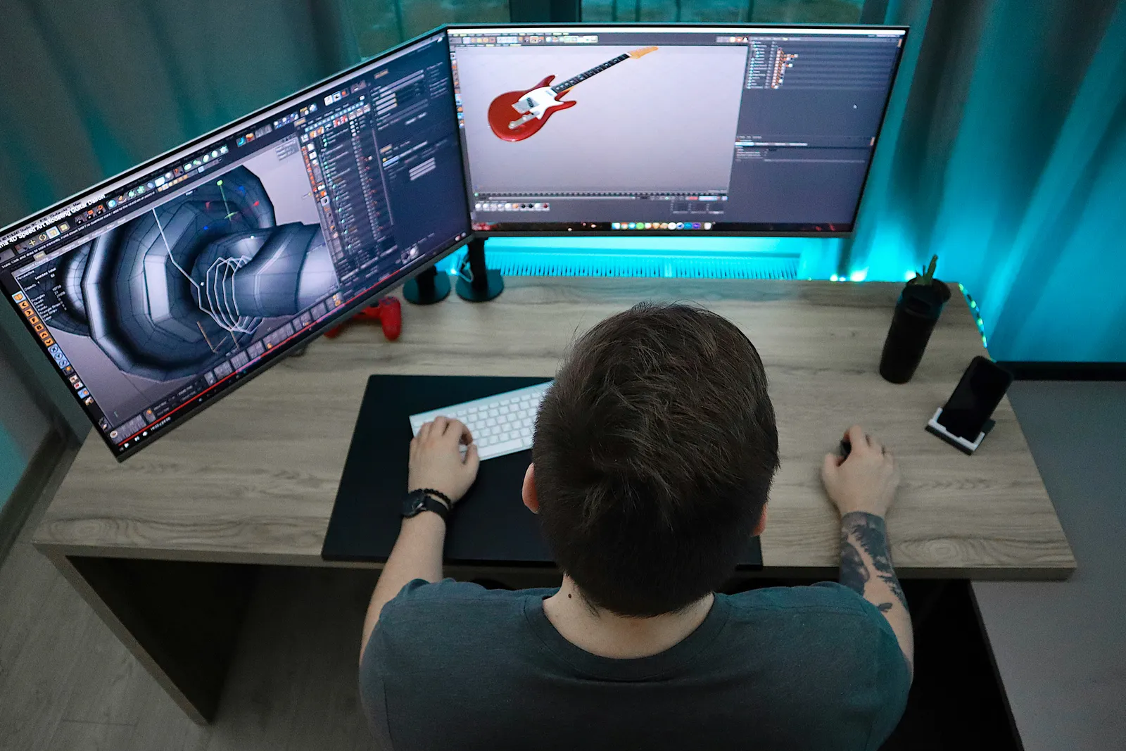 An artist working across two curved monitors with 3D modelling software open on both