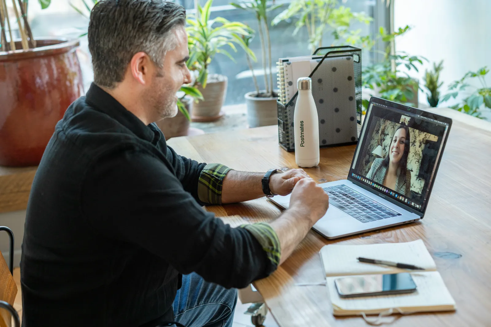 A designer joining a video call from a home desk with a laptop and notebook open