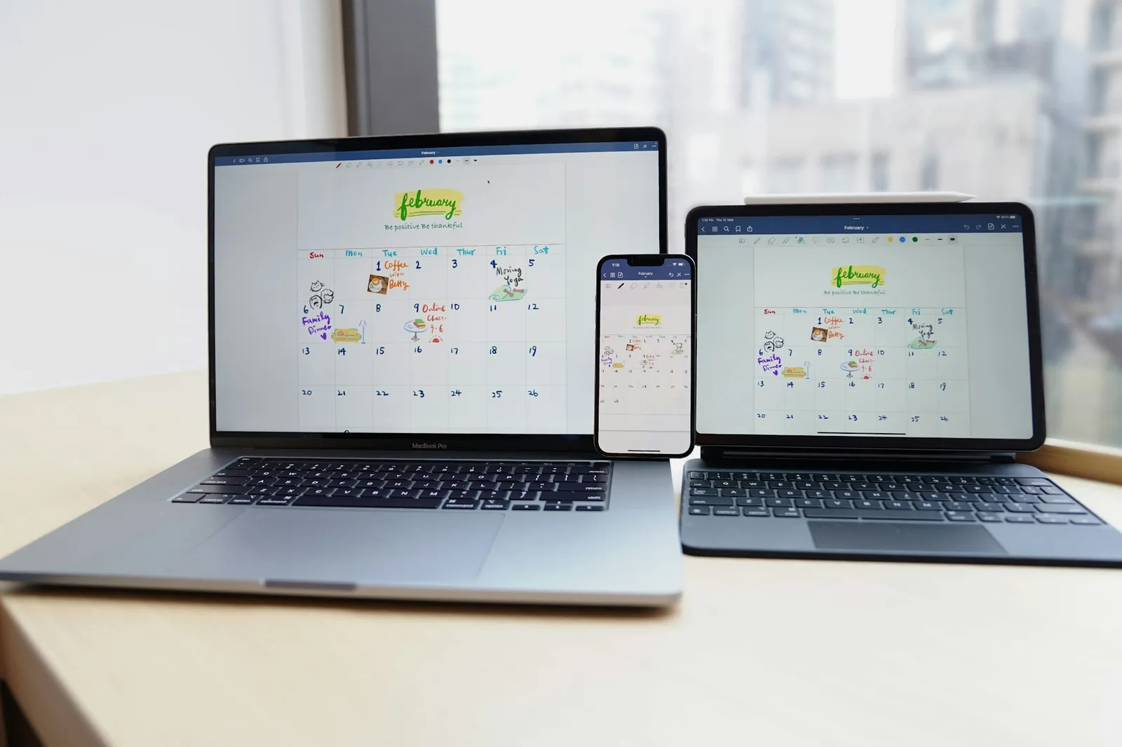 A MacBook, an iPhone and an iPad on a desk showing the same calendar page