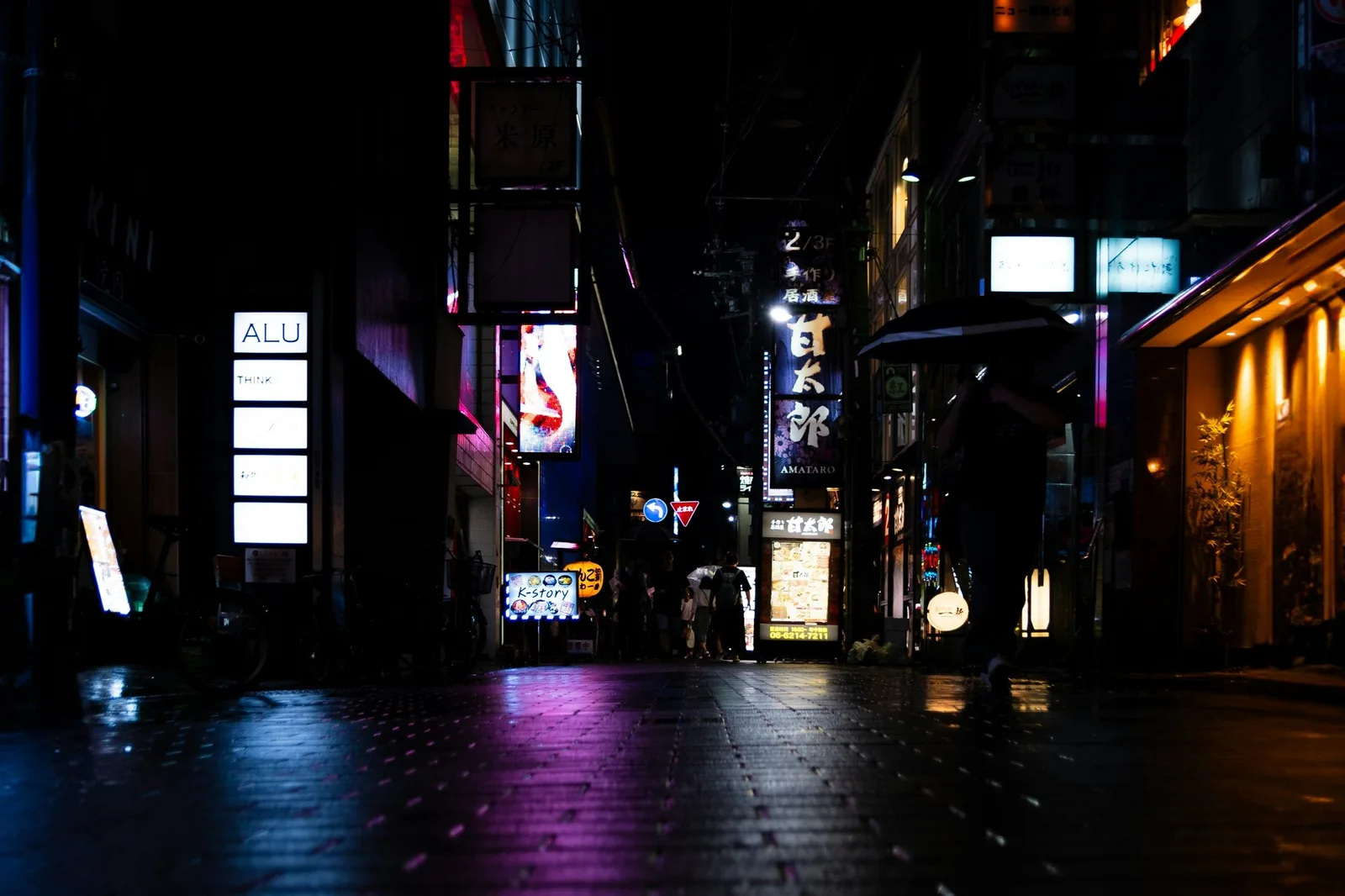 Dark city street at night lit by glowing neon signs in Osaka, Japan