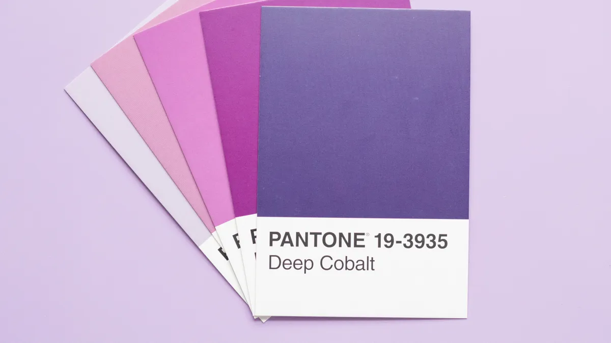 A fan of purple Pantone swatch cards ending in Deep Cobalt, laid on a lilac surface