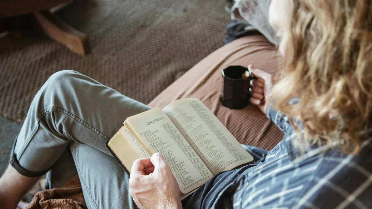 Person holding an open book alongside a black ceramic mug, close-up on the printed page