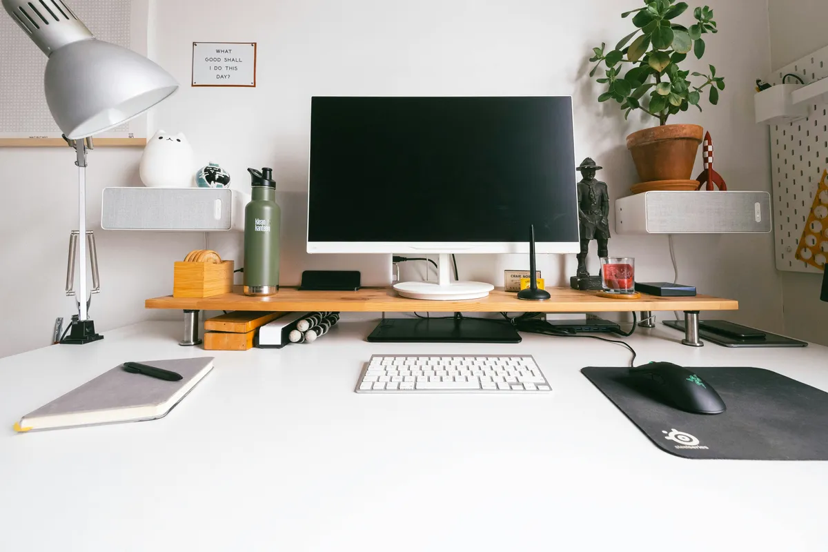 A silver iMac alone on a bare white wooden desk