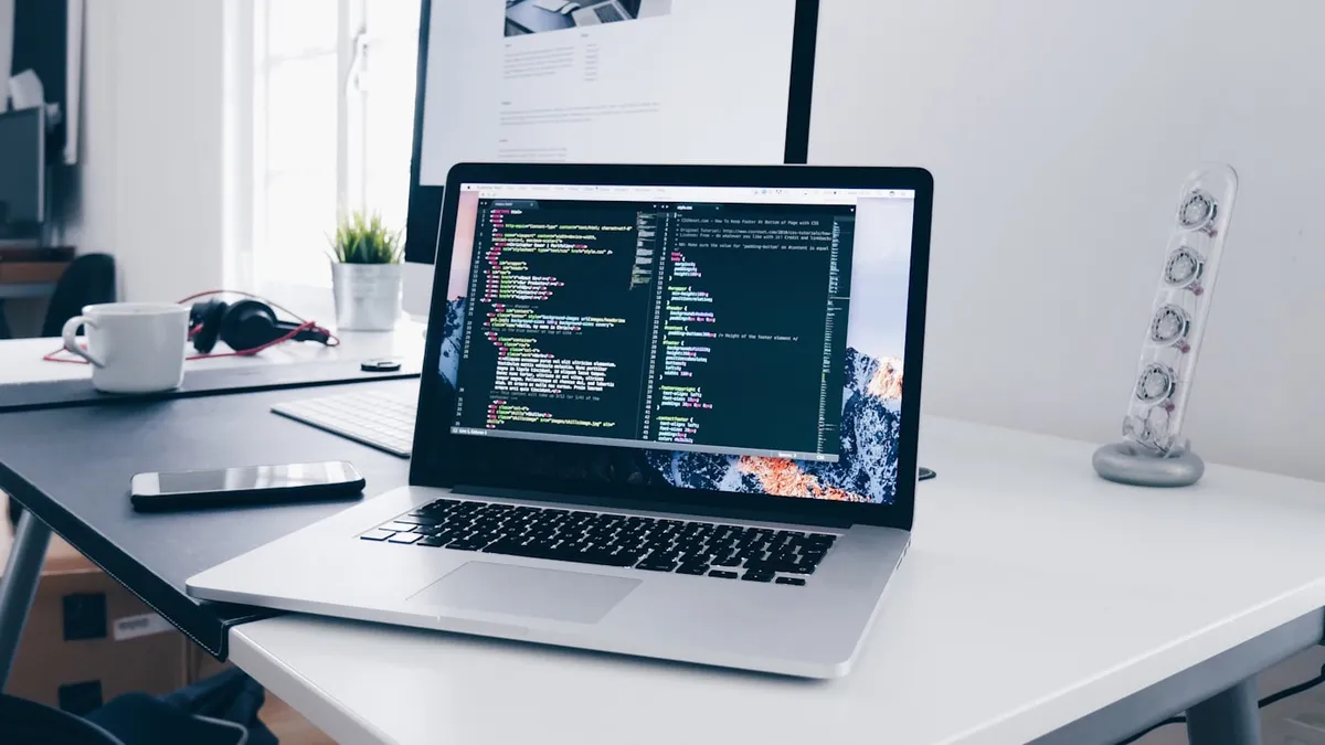 MacBook showing an interface on screen at a busy design workspace desk