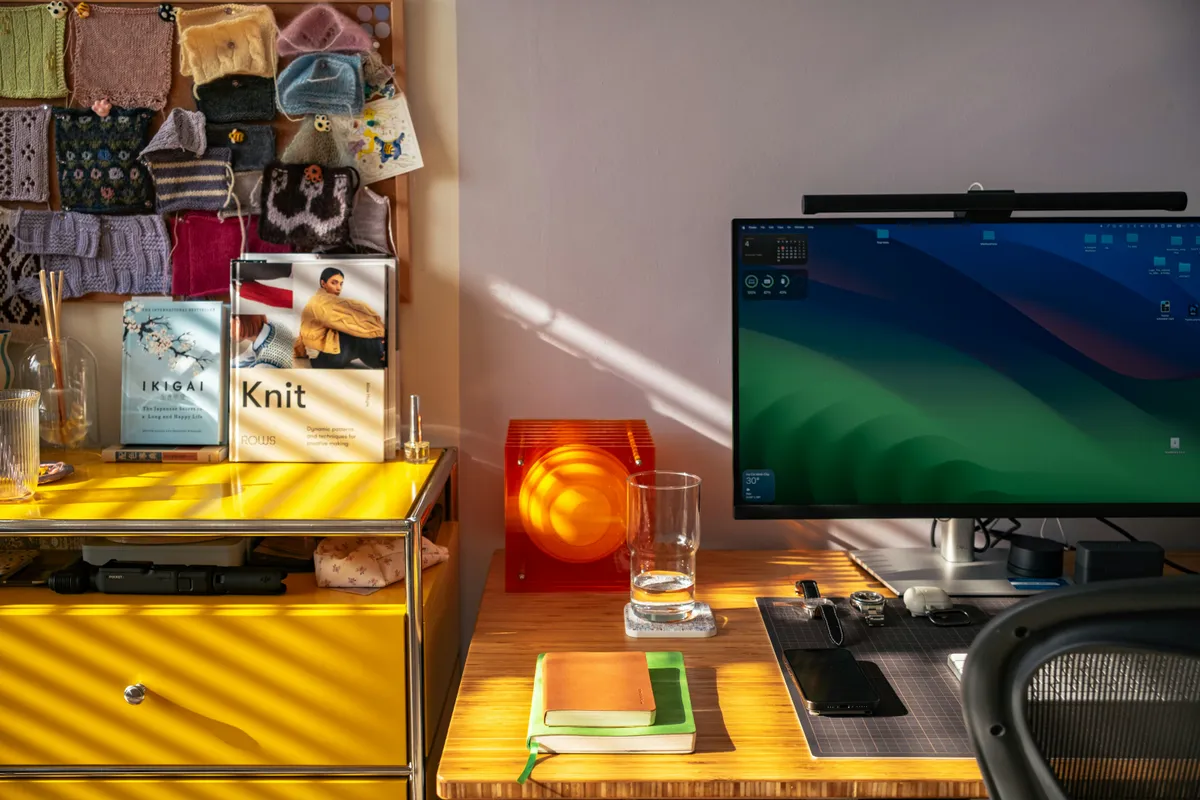 A sunlit home office desk with a monitor and stacked notebooks