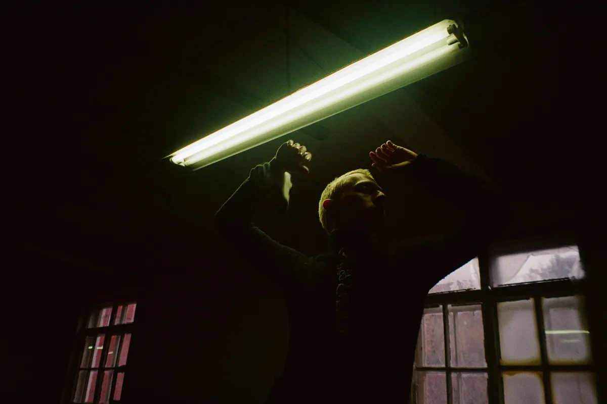 A figure with arms raised under a hard fluorescent tube
