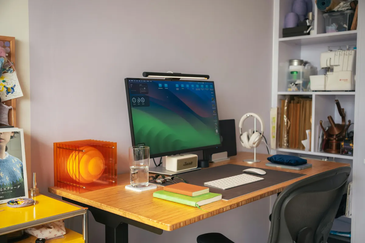 A monitor, keyboard and orange desk lamp on a wooden work surface