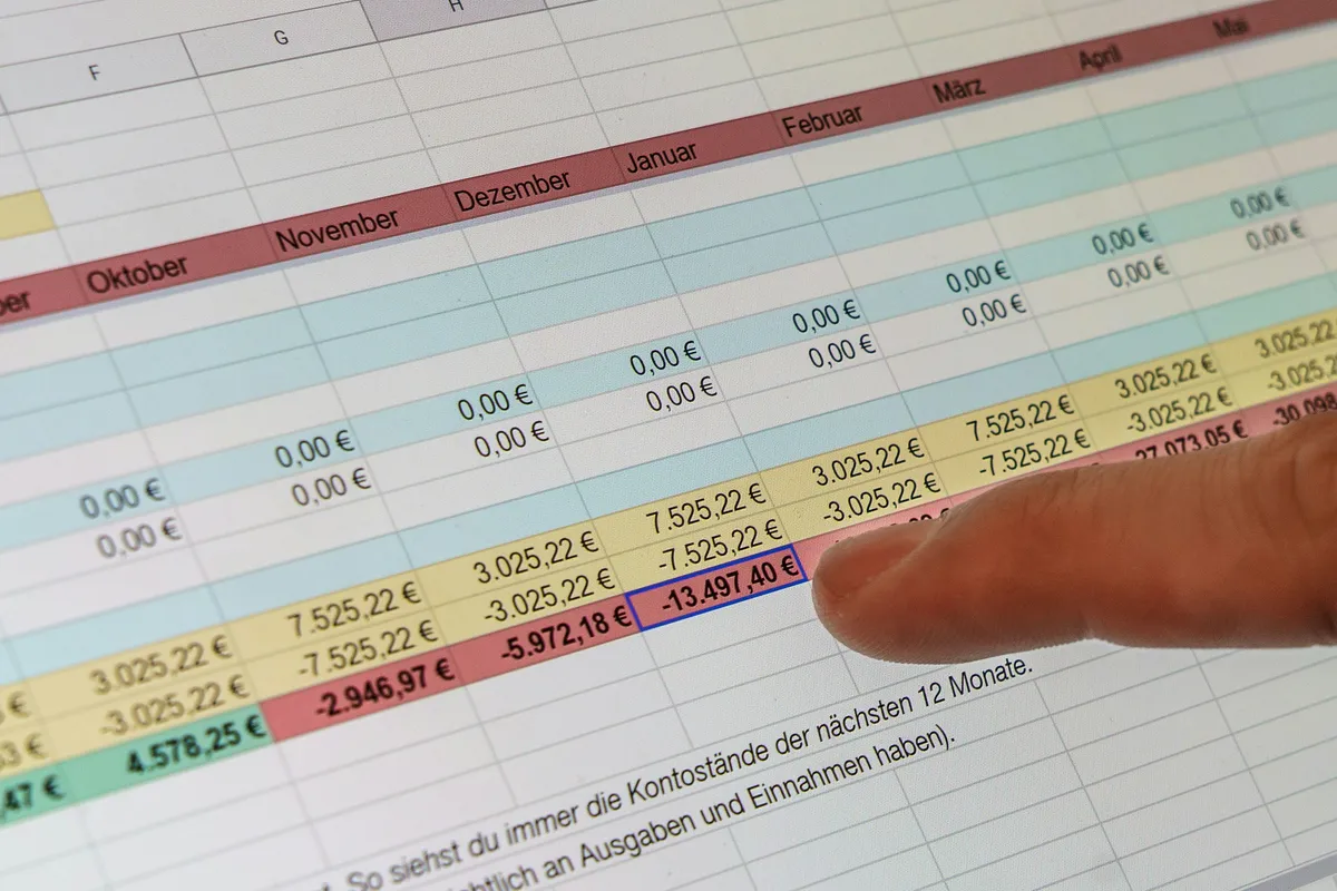 A finger pointing at a dense spreadsheet full of financial figures across many rows and columns