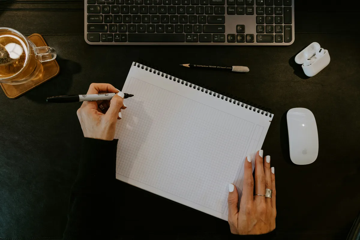 A person writing in a notebook next to a keyboard