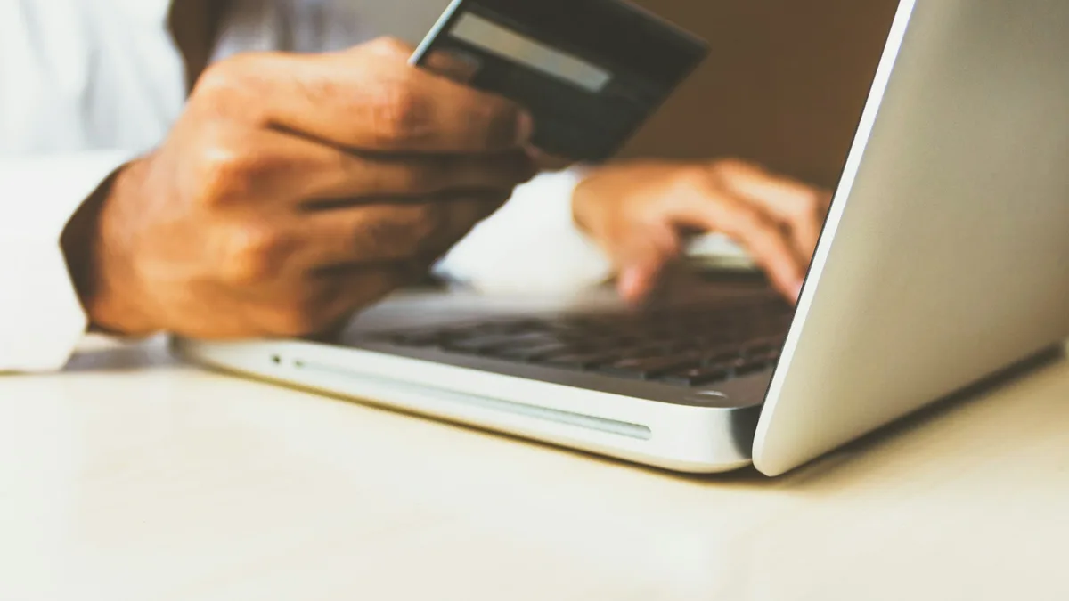 Person holding a payment card while using a laptop for online checkout