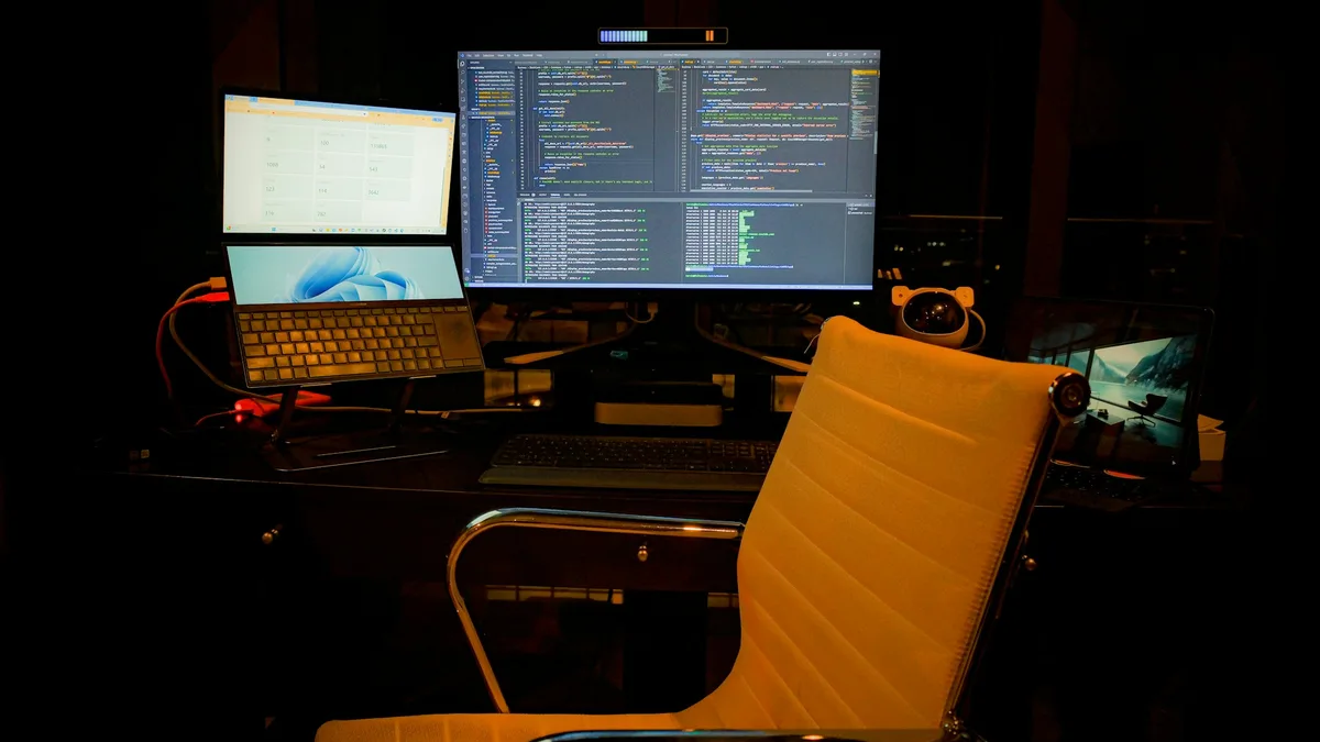 Computer desk with two monitors and a laptop showing design software