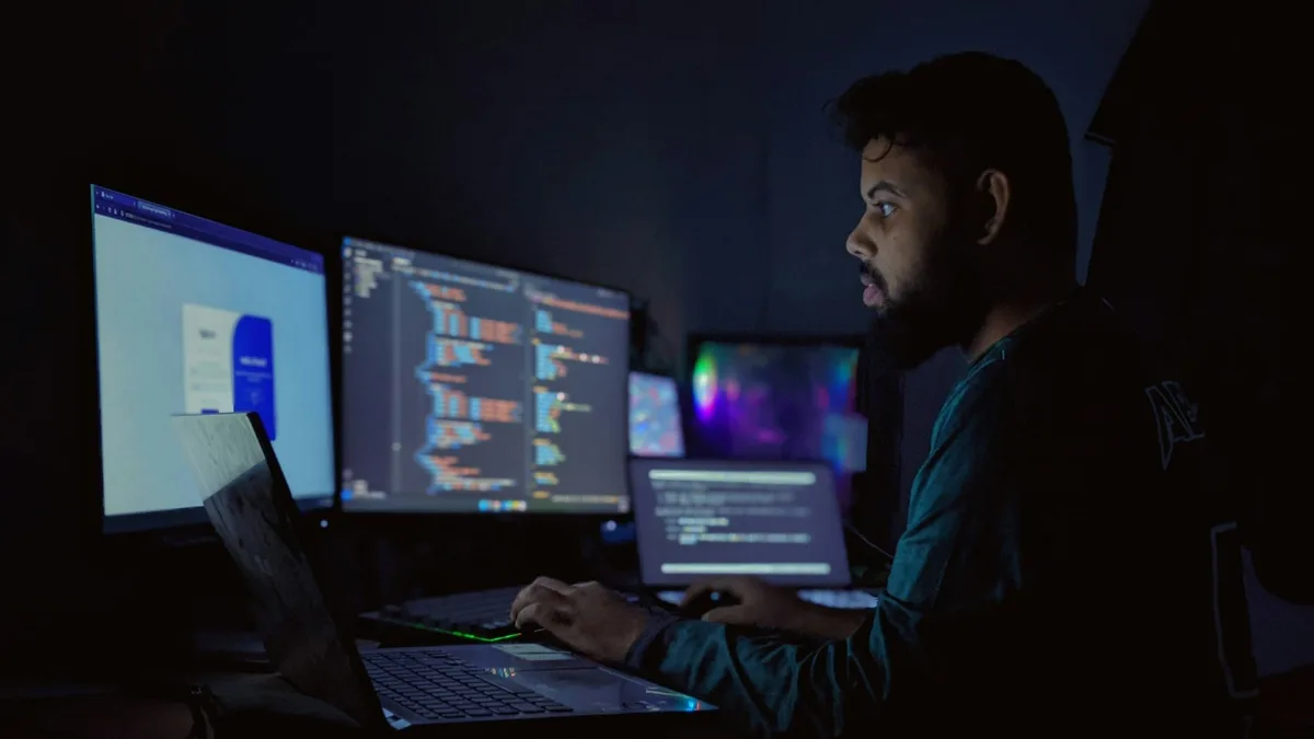 Person sitting at a desk in front of three computer monitors displaying work