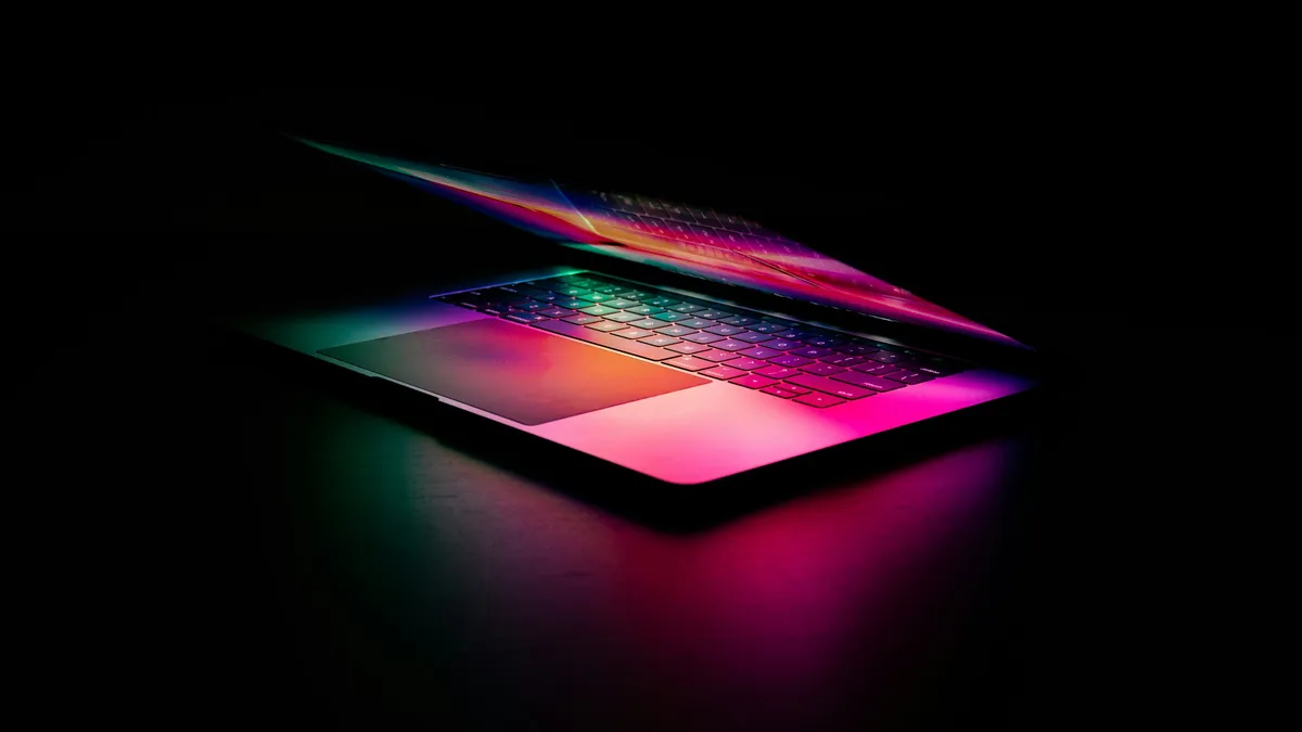 Laptop keyboard glowing pink and green in the dark, evoking AI-assisted design sessions