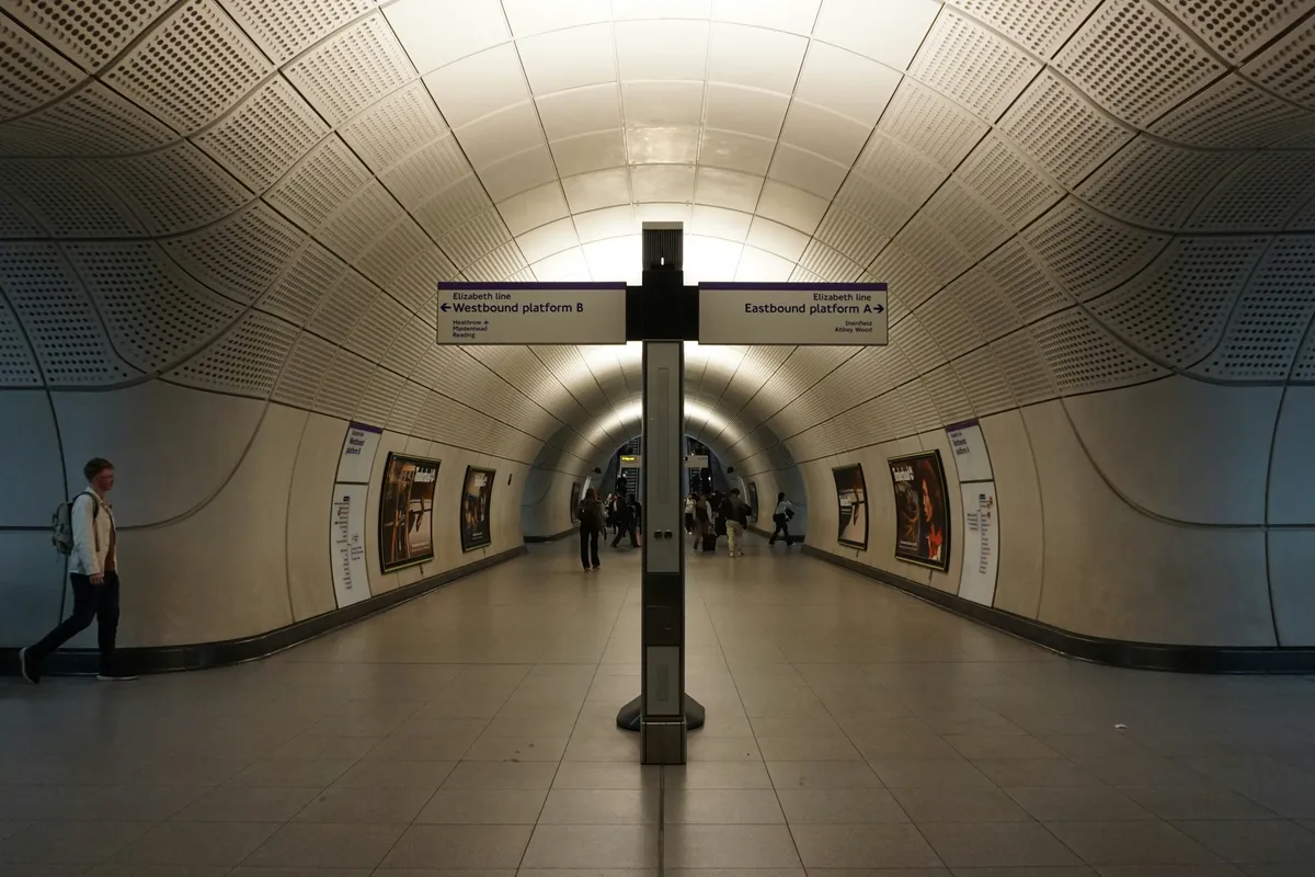 People walking through a lit tunnel past a central signpost