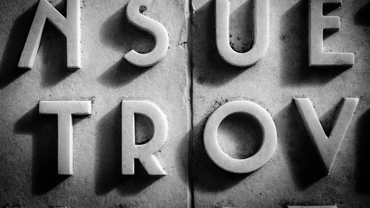 Monochrome close-up of raised letterforms spelling a word, showing typographic detail and shadow
