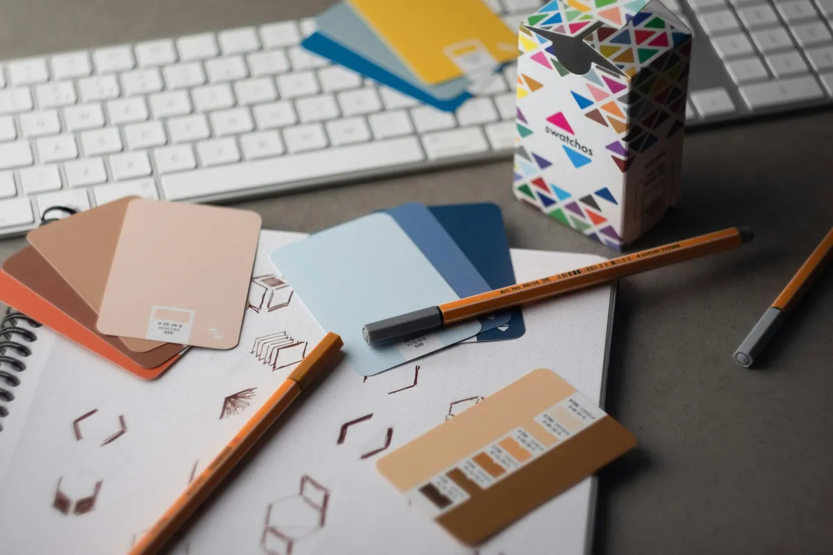A designer's desk with a keyboard, pencils and rows of printed colour samples