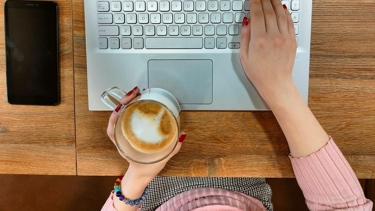 Person typing on a laptop keyboard with a cup of coffee nearby