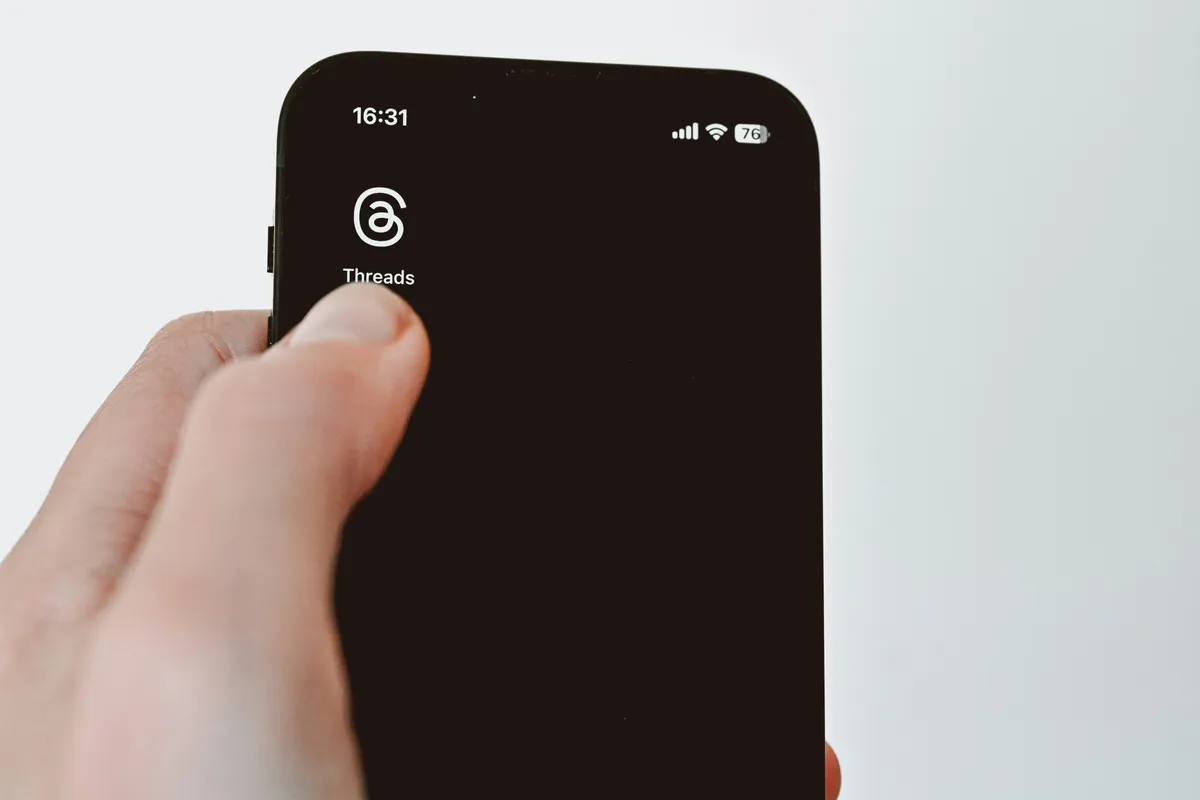 Hand holding a smartphone displaying an app screen, thumb positioned mid-tap