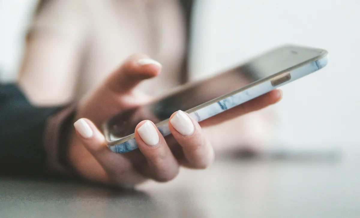 Person's hand tapping a smartphone screen with fingernails visible