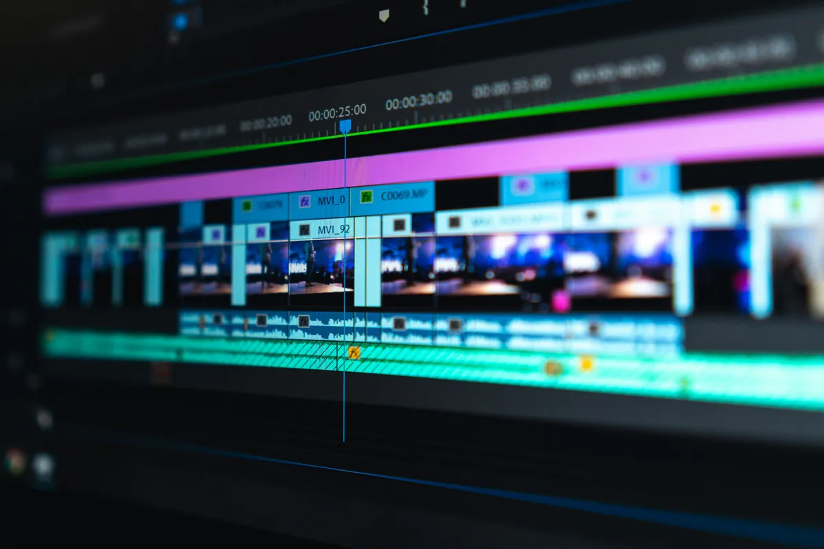 A multi track editing timeline with colour coded clips filling a dark monitor