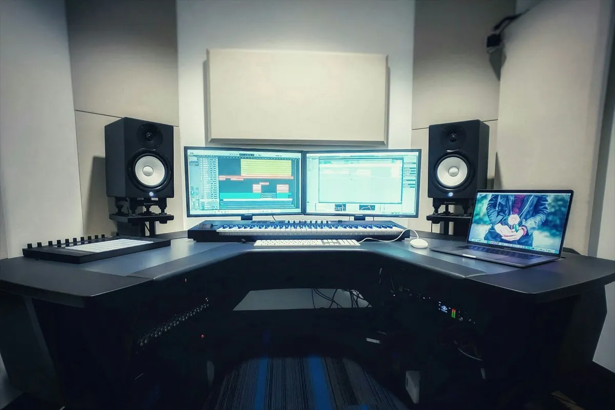A sound studio desk with two monitors, a MIDI keyboard and studio monitor speakers either side