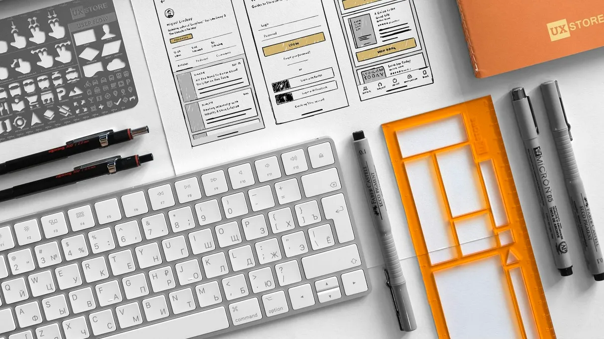 UX sketchbook with wireframe sketches open beside a MacBook on a designer desk