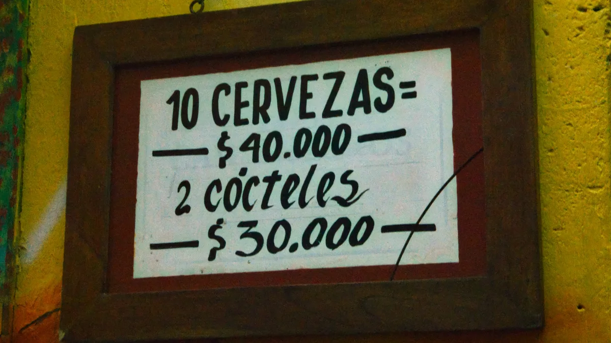 Chalkboard-style sign listing prices for beers and cocktails at a bar