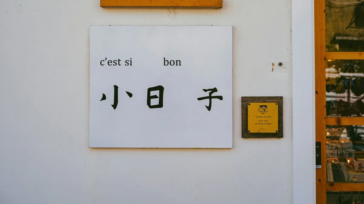 A shop sign mixing Latin lettering with large Chinese characters on a white wall