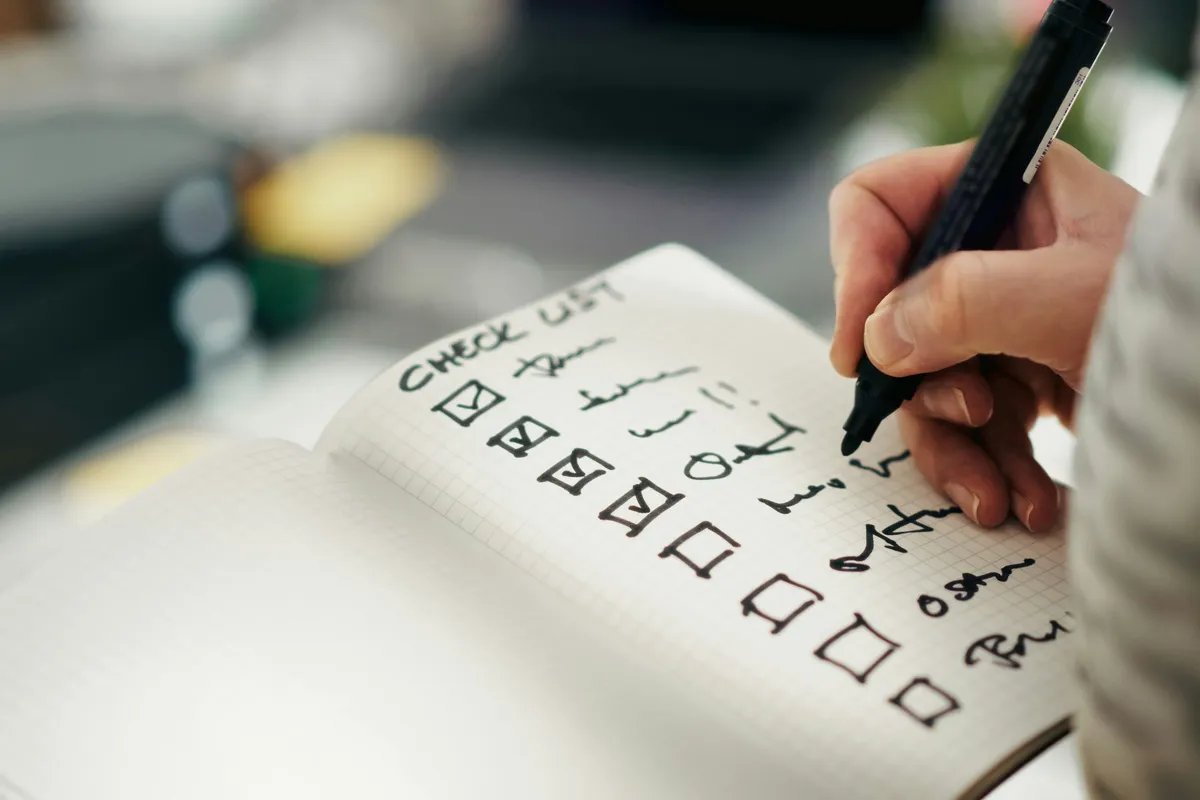 Hand ticking boxes on a handwritten checklist in a grid notebook