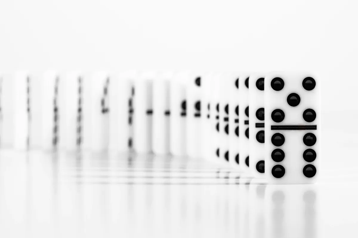 A long row of white dominoes receding into a soft white background, one tile sharp in front