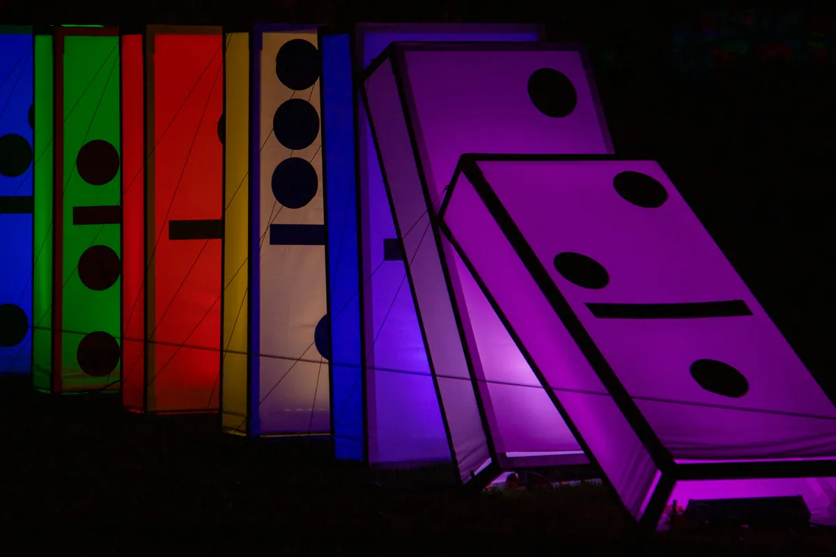 Oversized illuminated dominoes in green, red, yellow and purple tipping over in the dark