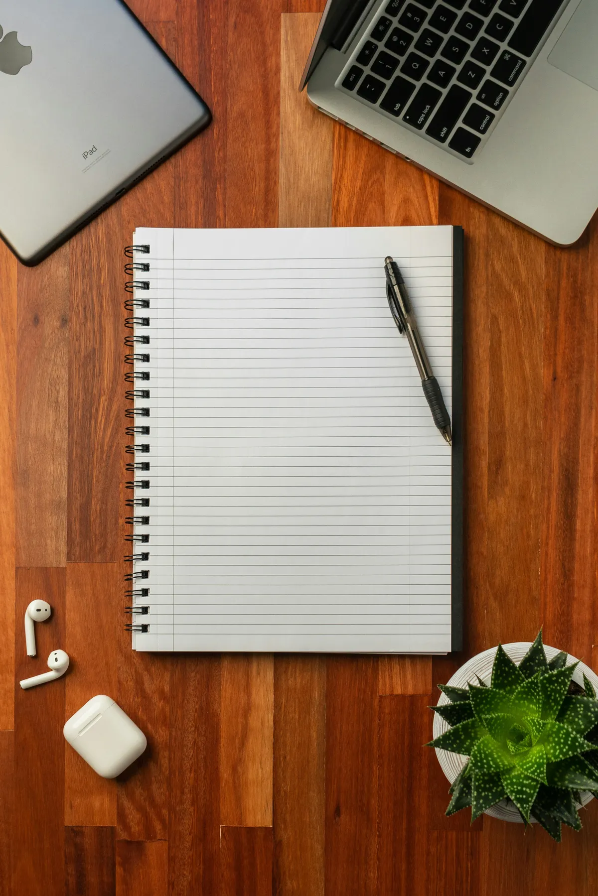 Notebook and pen next to a laptop on a wooden desk
