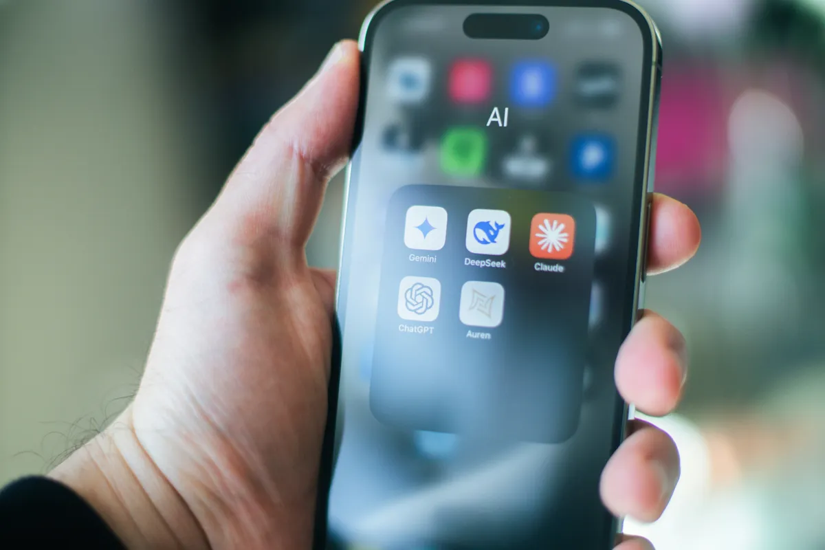 A hand holding a phone whose home screen is a grid of AI apps