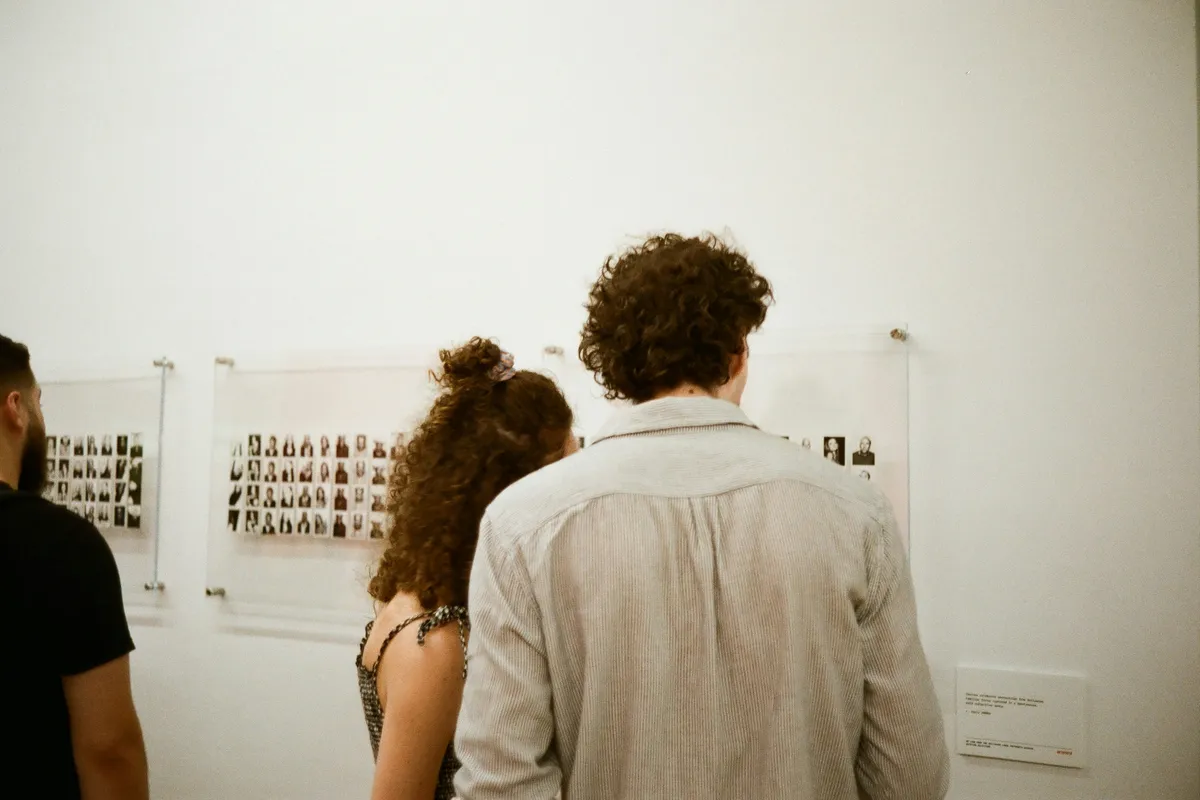 Two people leaning in to read small pictures on a white gallery wall