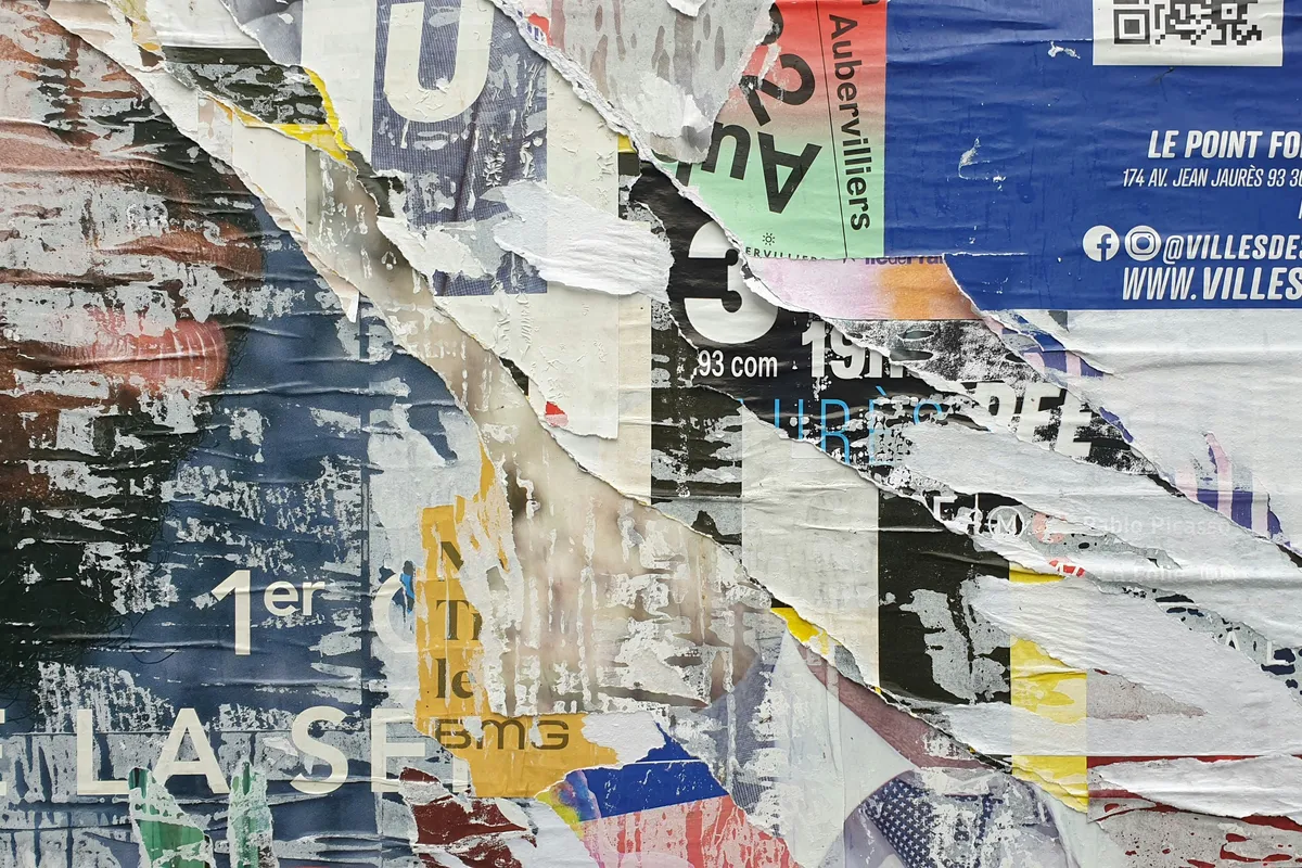 A wall of torn posters pasted over each other in layers