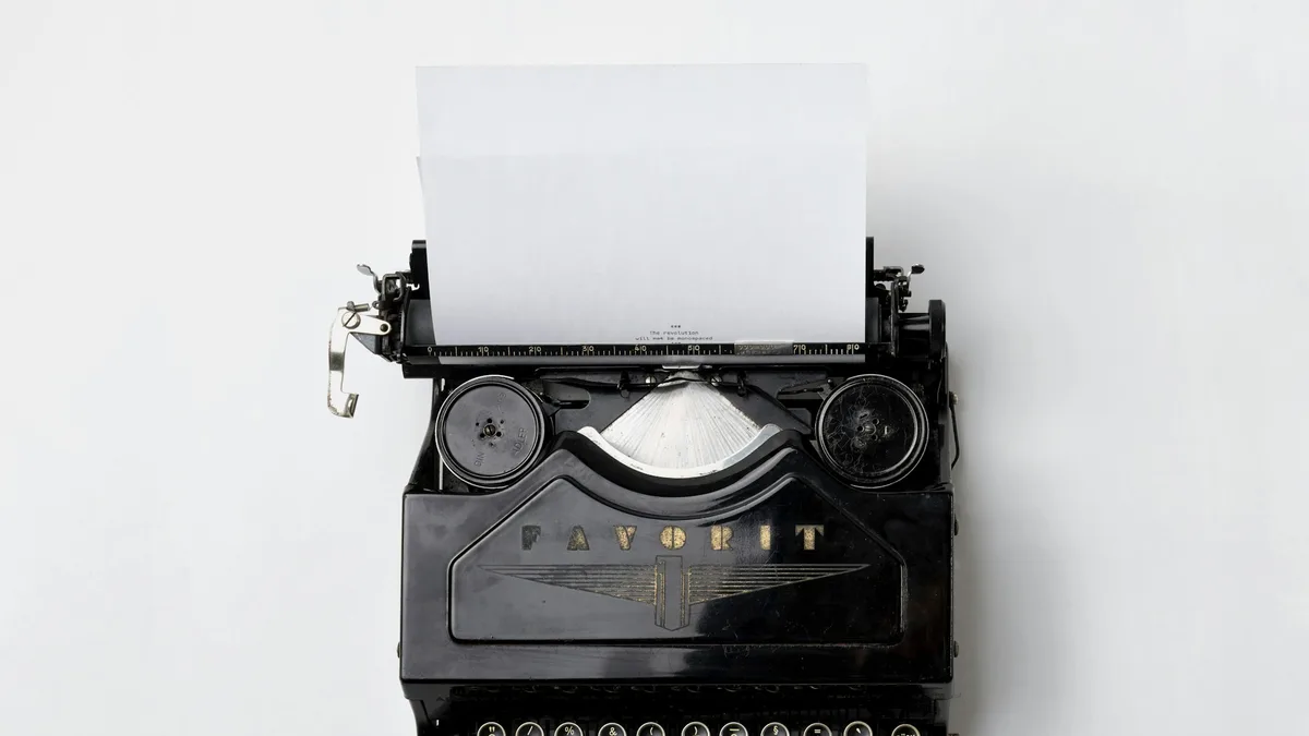 Black vintage typewriter with printer paper loaded, showing mechanical letterforms