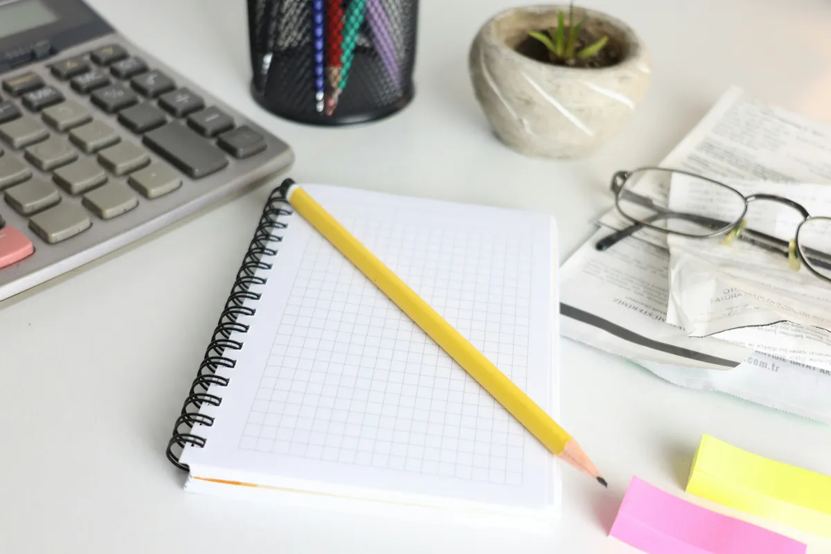 A desk with a calculator, a notebook, a pencil and a pair of glasses