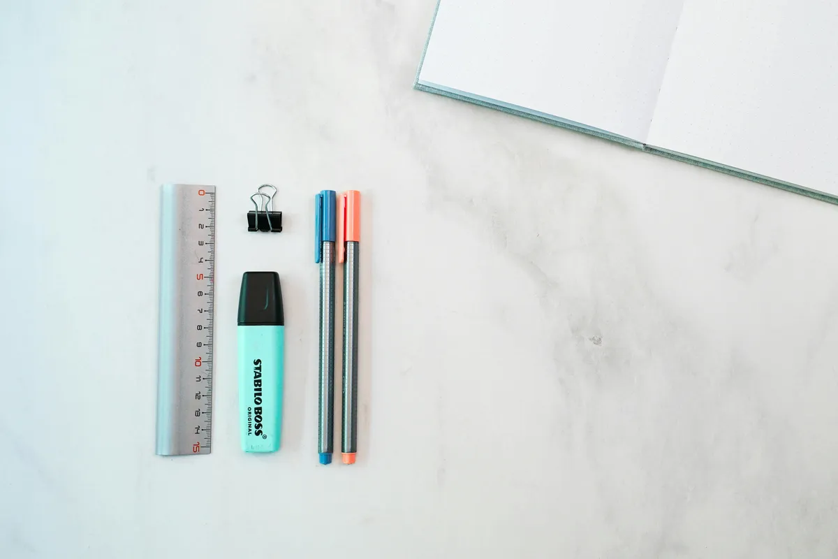 A notebook, pen, ruler and pencil laid out on a marble surface