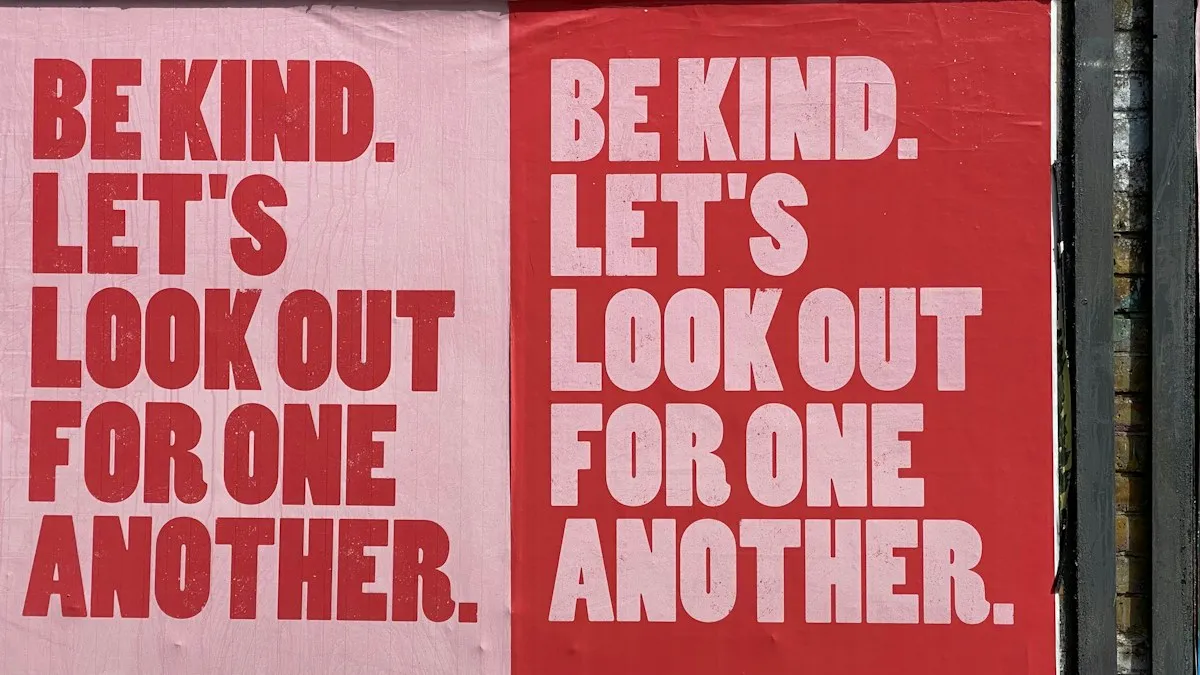 Two red and pink street posters repeating the words Be kind in heavy stacked capitals